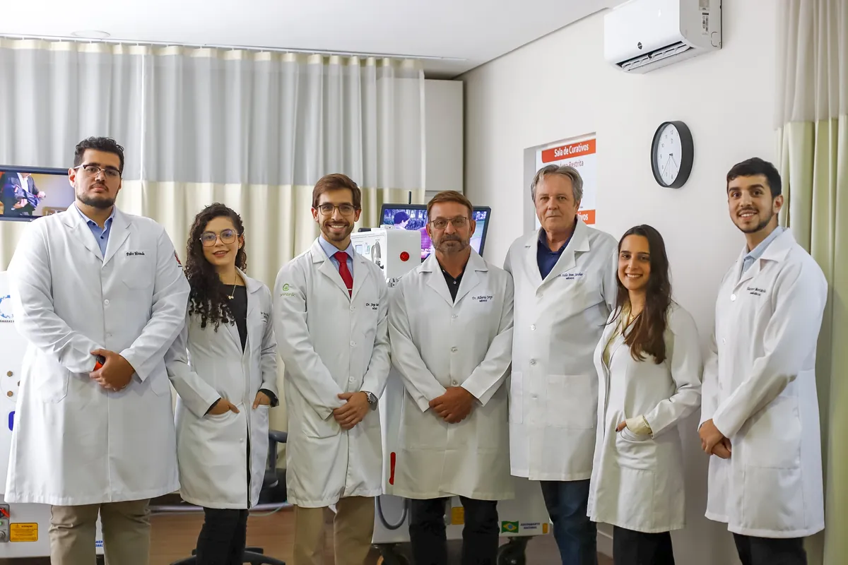 Sete médicos da equipe da BMH, de jaleco branco, lado a lado na sala das câmaras monoplace da unidade Asa Sul